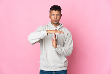 Young Brazilian man isolated on pink background making time out gesture