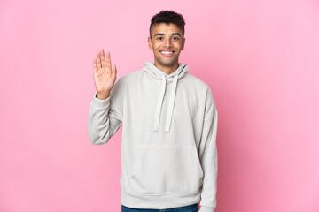 Young Brazilian man isolated on pink background saluting with hand with happy expression