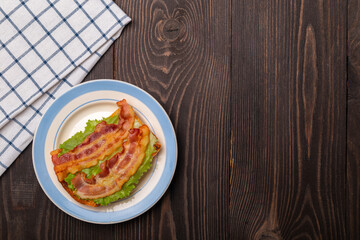 sandwich with fried bacon on a lettuce leaf on a dark wooden table top view