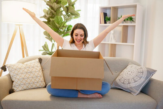 Woman sit on couch with joy opens carton box feel happy