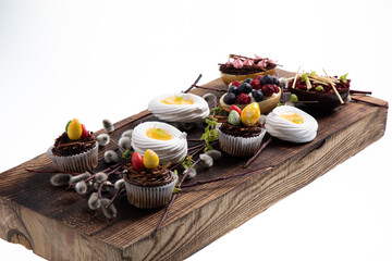 Selection of different sweet cupcakes, cookies and filled chocolate eggs on wooden board