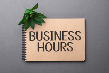 business hours text on craft colored notepad and green plant on the dark background