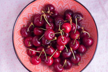 The berries of a young sweet cherry lie in a red, pink plate 