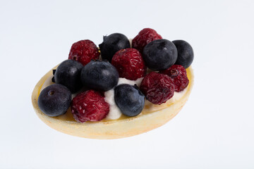 White chocolate egg filled with passion fruit mousse decorated with dried cranberries and fresh blueberries isolated on white