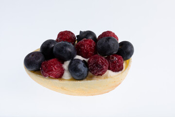 White chocolate egg filled with passion fruit mousse decorated with dried cranberries and fresh blueberries isolated on white