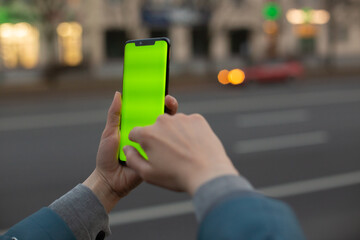 
Mock-up image of a woman using a smartphone with a green screen on the background of the road.