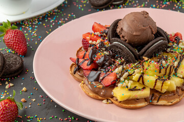 Heart waffle with pineapple and strawberry with gummy candy and ice cream on it.