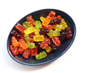 Multicolored gummy bears in black bowl on white background. Top view, copy space. Flat lay food. Chewing gummies on plate