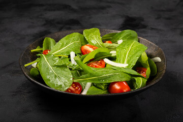 Arugula salad with tomatoes on dark background.