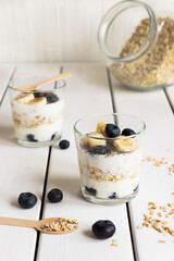 Two glasses with layered yogurt, oats and fruits, on white wooden table. Healthy breakfast, healthy lifestyle concept