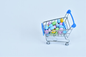 Shopping trolley with chokolate multicolored easter eggs on white background. Easter sale.