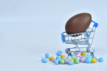 Shopping trolley with chokolate multicolored easter eggs on white background. Easter sale.