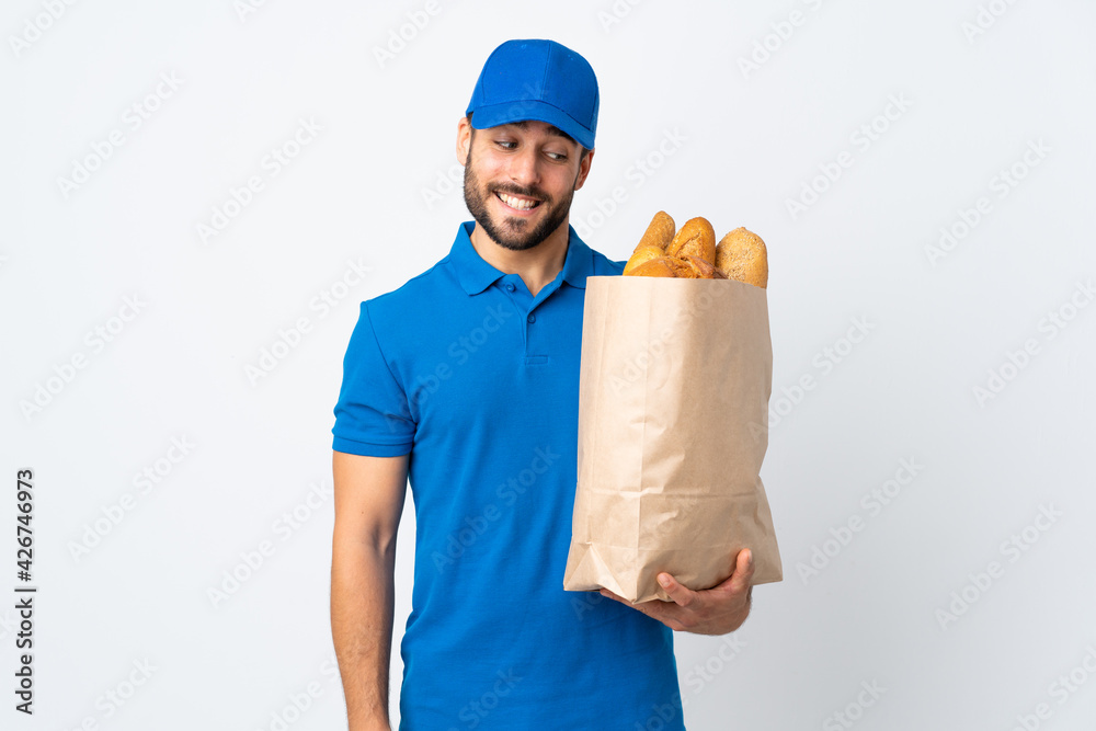 Poster Delivery man holding a bag full of breads isolated on white background with happy expression