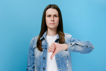 Dissatisfied young female showing thumbs down gesture, serious brunette woman customer giving...