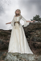 Fototapeta premium A gorgeous woman, a mythical creature, a queen, she is in a white dress, on large stones, in the autumn forest The concept of a fairy tale, legend, theater, cinema