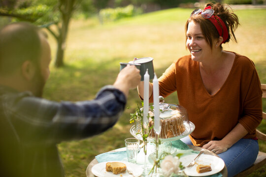 Happy couple enjoying tea and cake at table in sunny garden