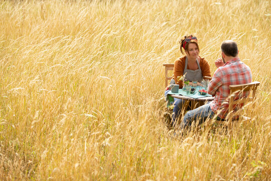 Couple enjoying fruit at table in sunny summer field of tall grass