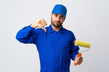 Painter man holding a paint roller isolated on white background showing thumb down with negative expression