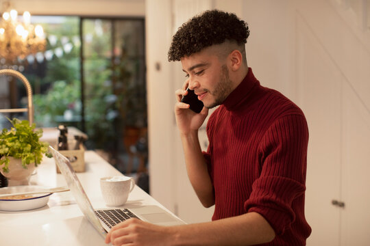 Young man working from home talking on smart phone at laptop
