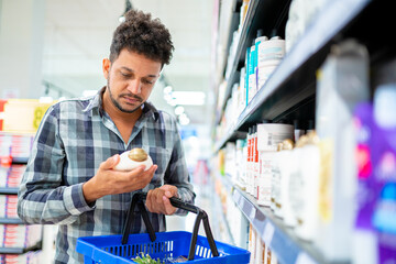 Latin American male customer choosing a men's hair product from the supermarket shelf. Male...