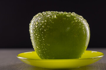Fresh green apple on a saucer with water drops on a black background.