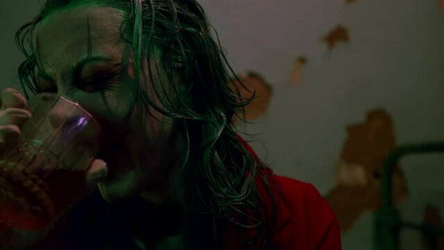 Close-up portrait of a woman with clown makeup laughing while drinking alcohol
