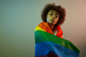 lgbtq concept. Positive caucasian girl with afro curly hair holding rainbow flag isolated in studio