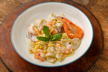 Pasta with shrimps in a creamy sauce, garnished with spinach on a gray plate on a wooden table on a round stand.