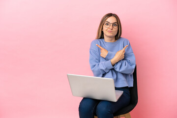 Naklejka premium Young woman sitting on a chair with laptop over isolated pink background pointing to the laterals having doubts