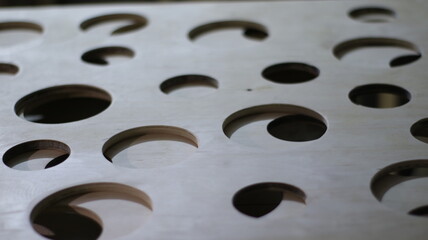 wooden canvas with round holes in dim lighting as a textured embossed background, abstract geometric space, natural wood material with cut through circles as a graphic resource