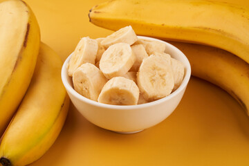 White cup with sliced bananas on a yellow background. Tropical fruits, healthy food, vitamins