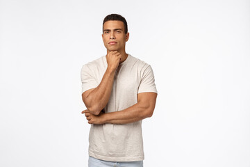 Skeptical, suspicious handsome strong man in t-shirt, have doubts, hold arm under chin, squinting...