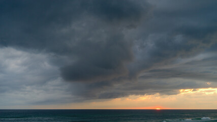 Fototapeta na wymiar Sunset with dramatic dark storm clouds over the ocean