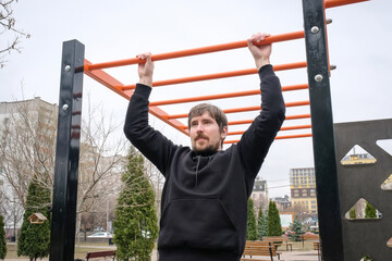 Obraz premium Young man doing pull-up exercises on the playground. Concept of sport and healthy lifestyle