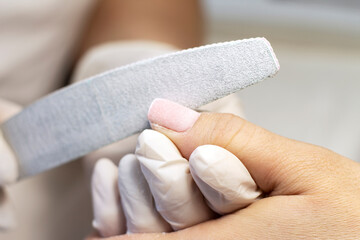 Manicure coating and strengthening of natural nails with artificial material gel in a beauty salon by a specialist. Close-up. Space for text
