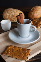 A cup of aromatic black coffee and coffee beans on the table with cinnamon sticks. Morning espresso coffee for breakfast in a beautiful white cup. Against the background of French buns. 