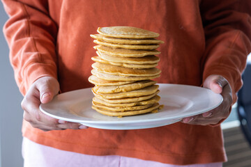 Cropped midsection of a  girl in a sweatshirt holding a plate with a towering stack of pancakes