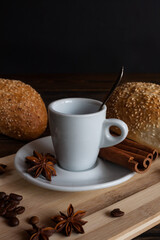 A cup of aromatic black coffee and coffee beans on the table with cinnamon sticks. Morning espresso coffee for breakfast in a beautiful white cup. With a delicious donut in the background.
