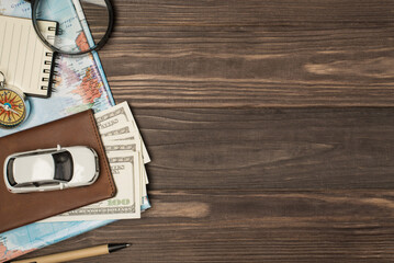 Above photo of brown passport wit money dollars cash inside car map magnifier compass notepad and pen isolated on the wooden backdrop with copyspace