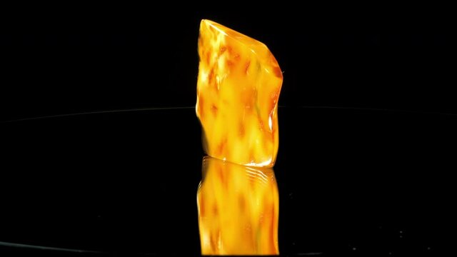 Thin amber stone with orange and terracotta elements rotates under electric light at exhibition closeup. Concept jewellery