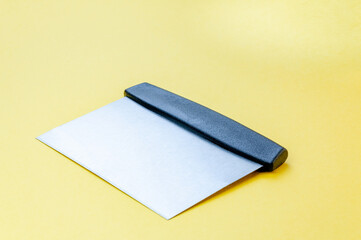 Metal dough scraper knife over bright yellow surface background. Stainless steel flat dough scraper with plastic handle