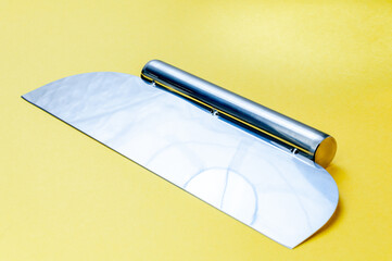 Metal dough scraper knife over bright yellow surface background. Stainless steel flat dough scraper