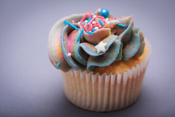 Close up of multicolored creamy cupcake with decorations with colorful stars, delicious and fabulous. Top view on gray background. Concept of birthday, celebration, sweet.