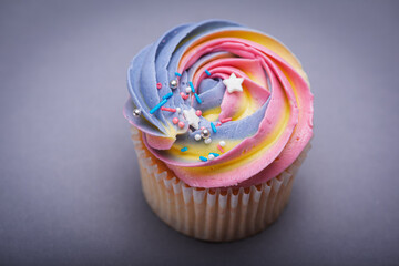 Close up of multicolored creamy cupcake with decorations with colorful stars, delicious and fabulous. Top view on gray background. Concept of birthday, celebration, sweet.