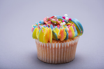 Close up of multicolored creamy cupcake with decorations with colorful stars, delicious and fabulous. Top view on gray background. Concept of birthday, celebration, sweet.