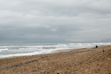 Lonely beach on a rainy sunset, with some fishermen in the background.