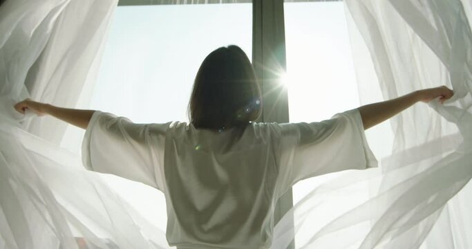 Young woman pulling curtains and enjoying view in large window. Girl starting new day with fresh thoughts. New beginnings, vacation 4k footage
