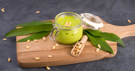 Pesto made from wild garlic, pine nuts and feta cheese in a glass, with fresh leaves on a dark...