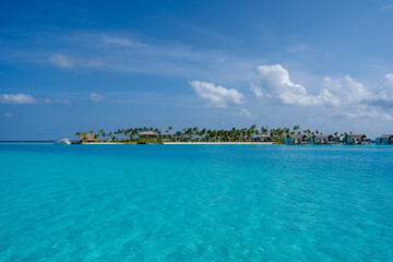 Blick auf eine Insel der Malediven, mit Palmen, Strand, Overwater Bungalows und dem kristallklaren und türkisblauen Wasser