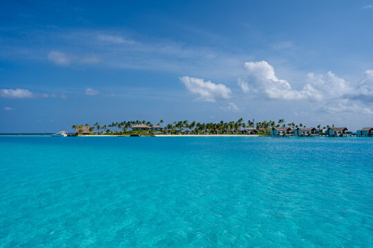 Blick auf eine Insel der Malediven, mit Palmen, Strand, Overwater Bungalows und dem kristallklaren und t&uuml;rkisblauen Wasser